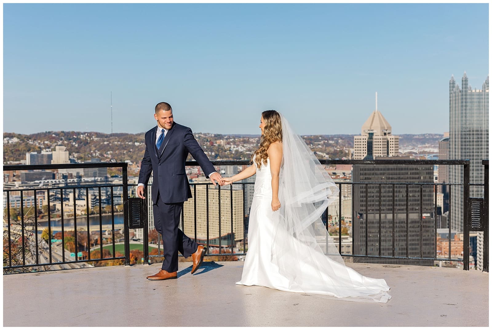 an image of a bride and groom holding hands on a bright sunny day featuring a city skyline in the background